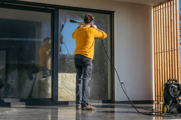 Man using a high pressure squirt gun to clean the window of the apartment on sunny day.